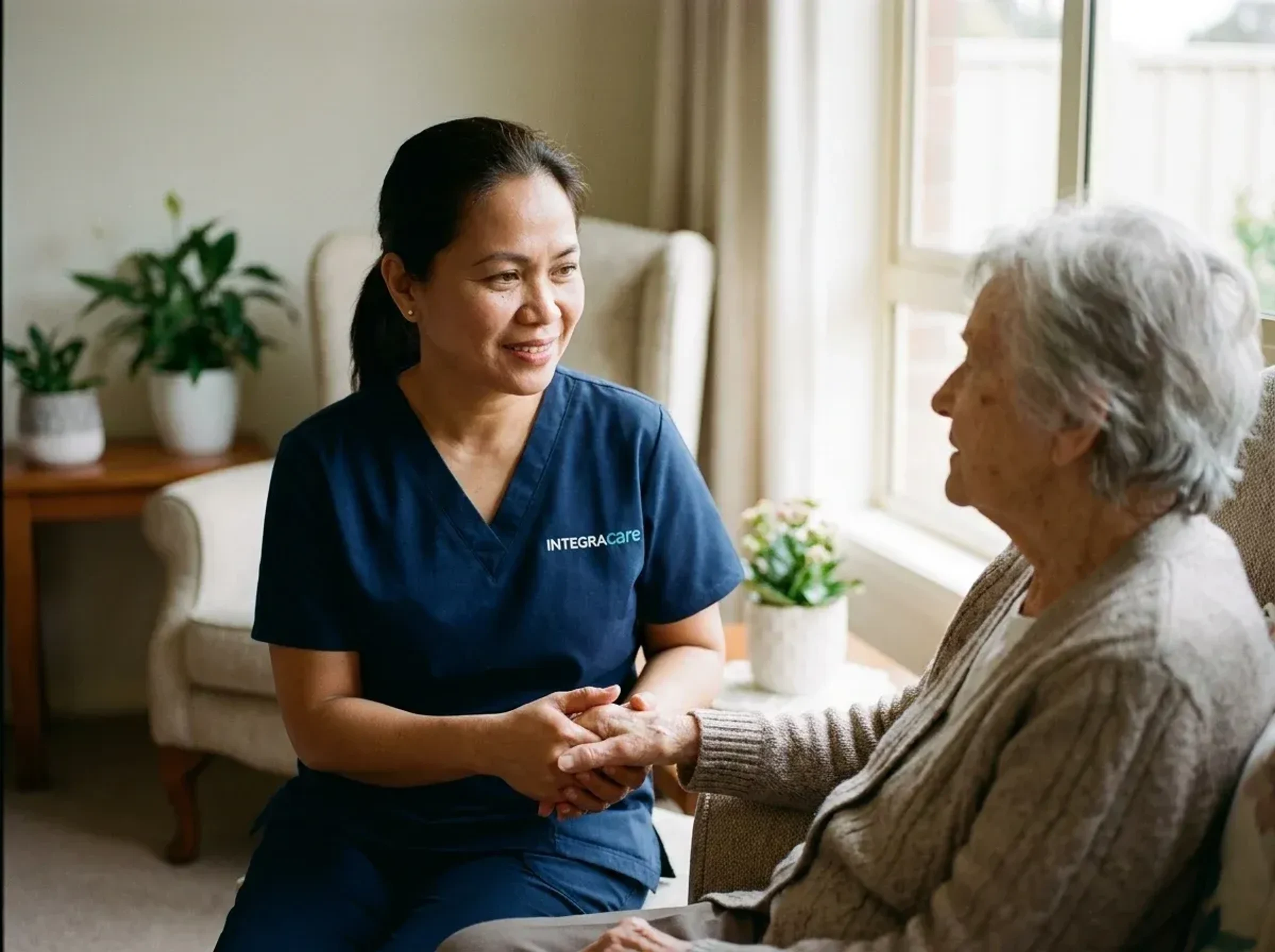 Eldercare caregiver holding hands with an older client by a sunlit window